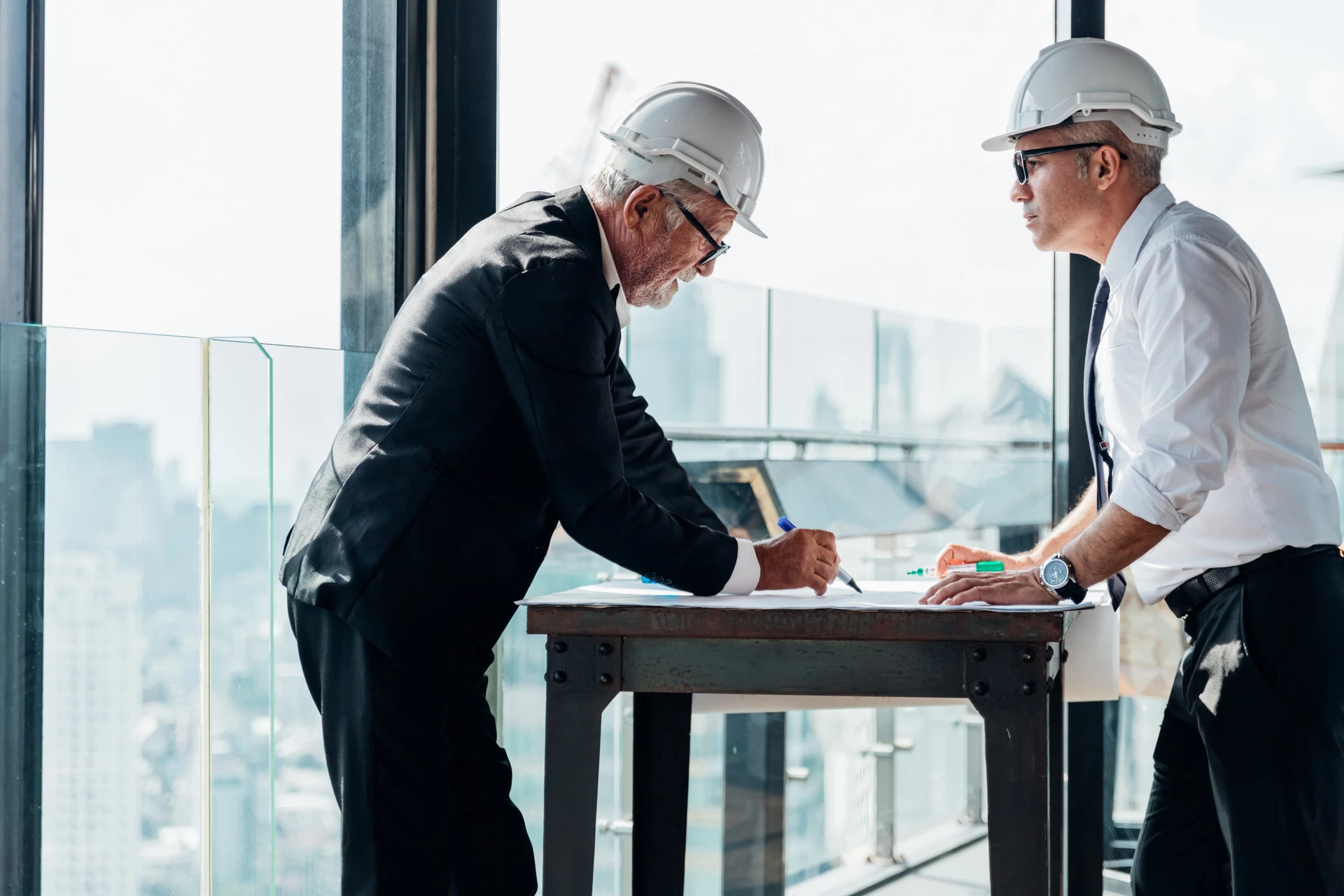 Two industrial engineer wear safety helmet engineering working and talking with drawings inspection modern city background. Industry, Engineering, construction concept. With copy space for your text